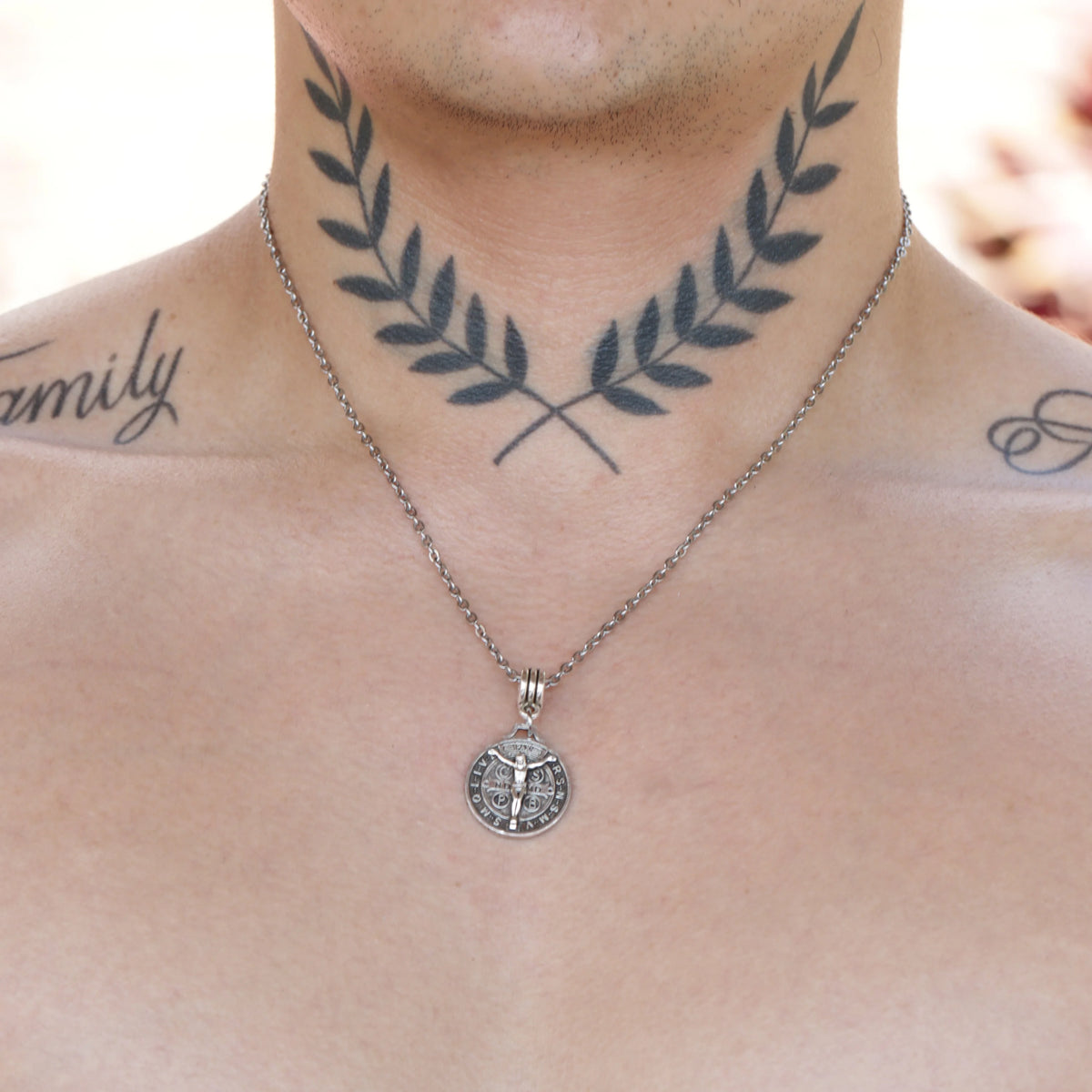 Crossed laurel wreath tattoo on a neck with a silver pendant necklace.