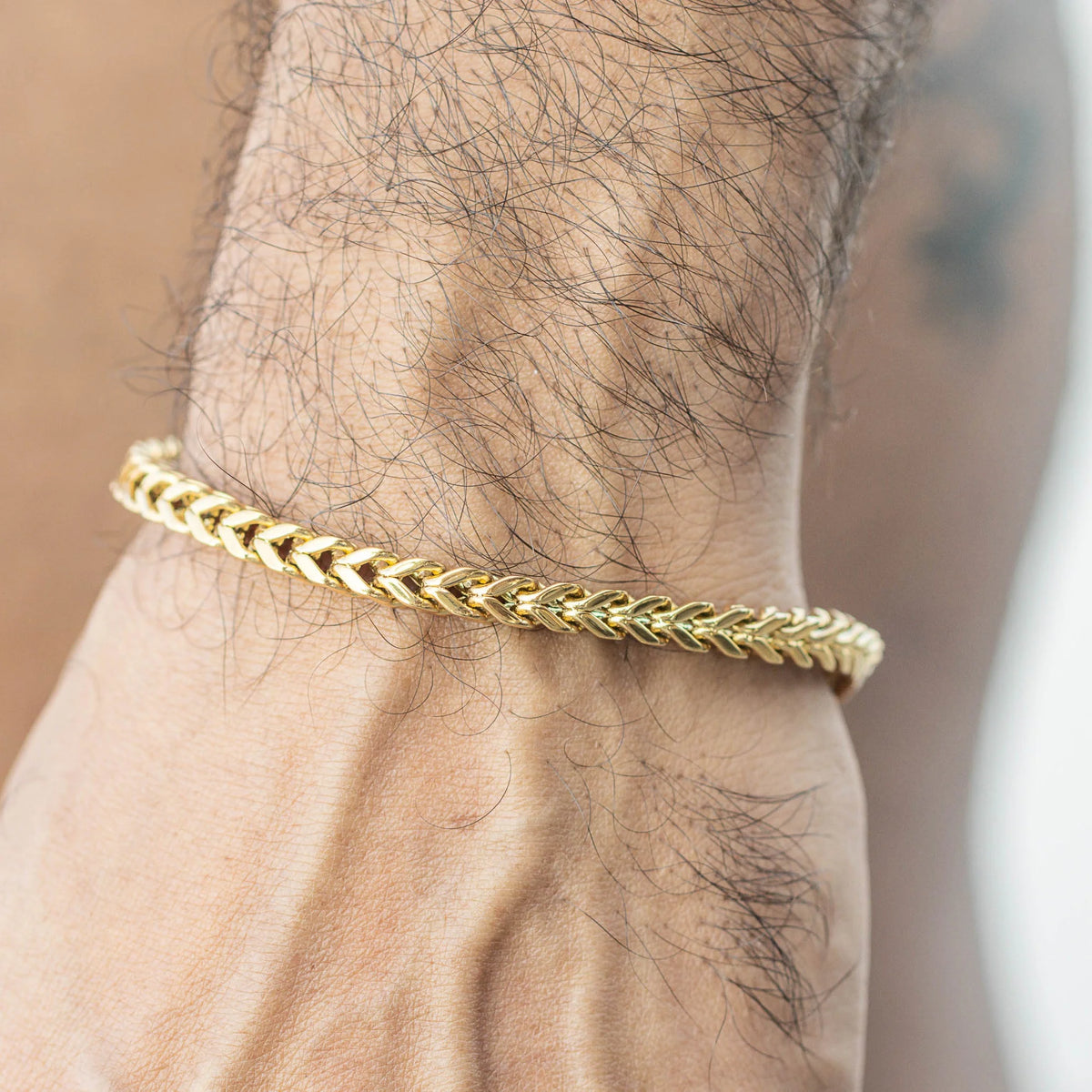 Gold braided chain bracelet worn on a wrist.