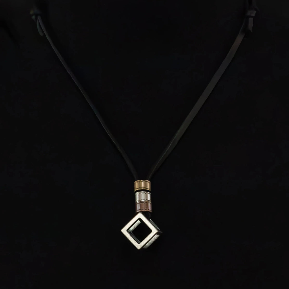 Pendant necklace with a square-shaped charm on a black cord.