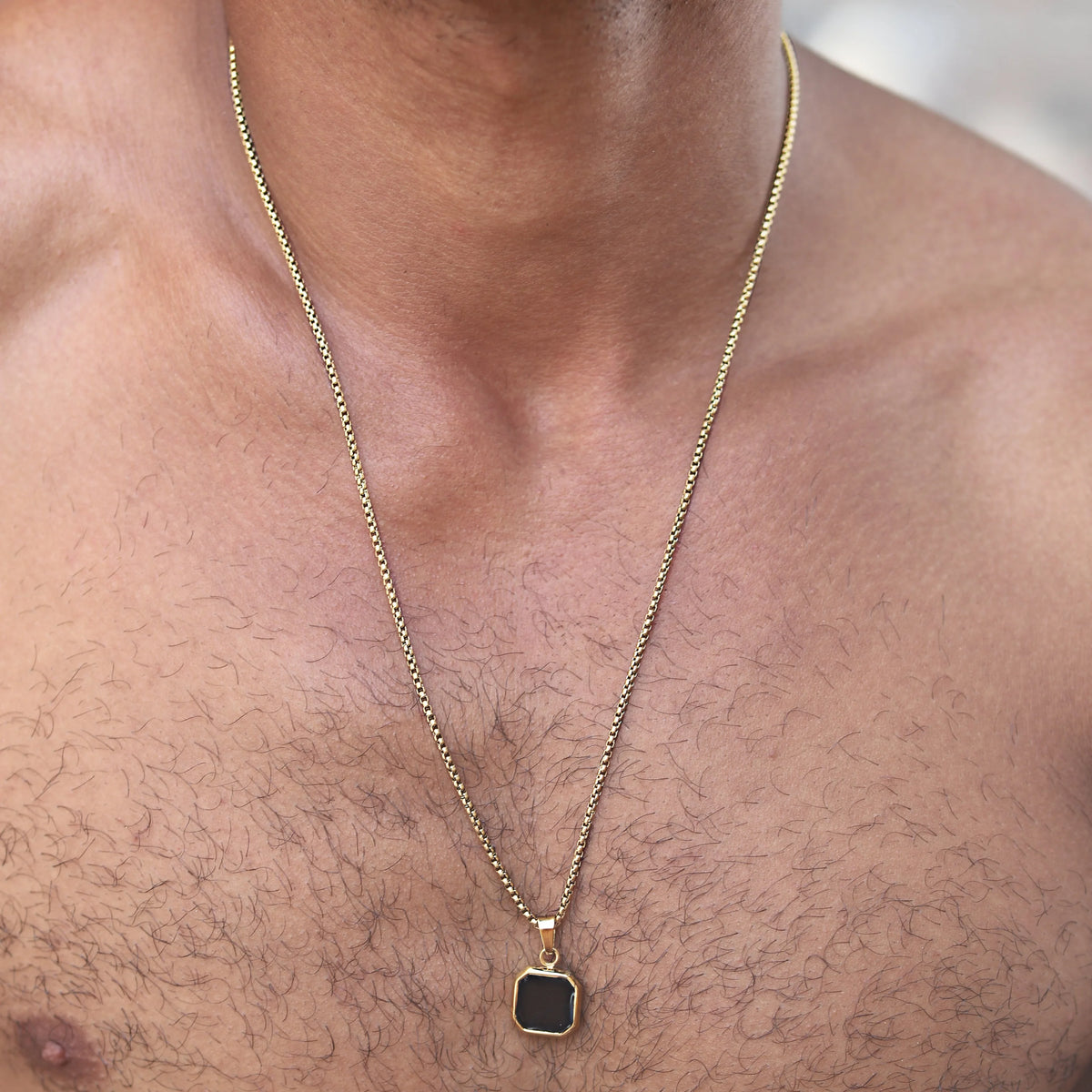 Gold chain necklace with a square black pendant.