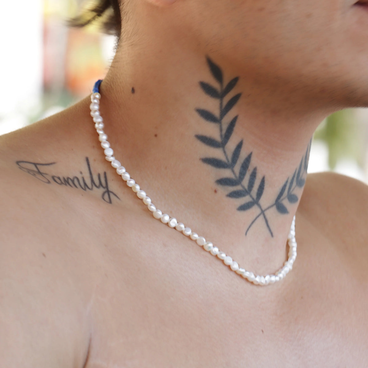 Pearl necklace worn with visible tattoos on the neck and collarbone area.