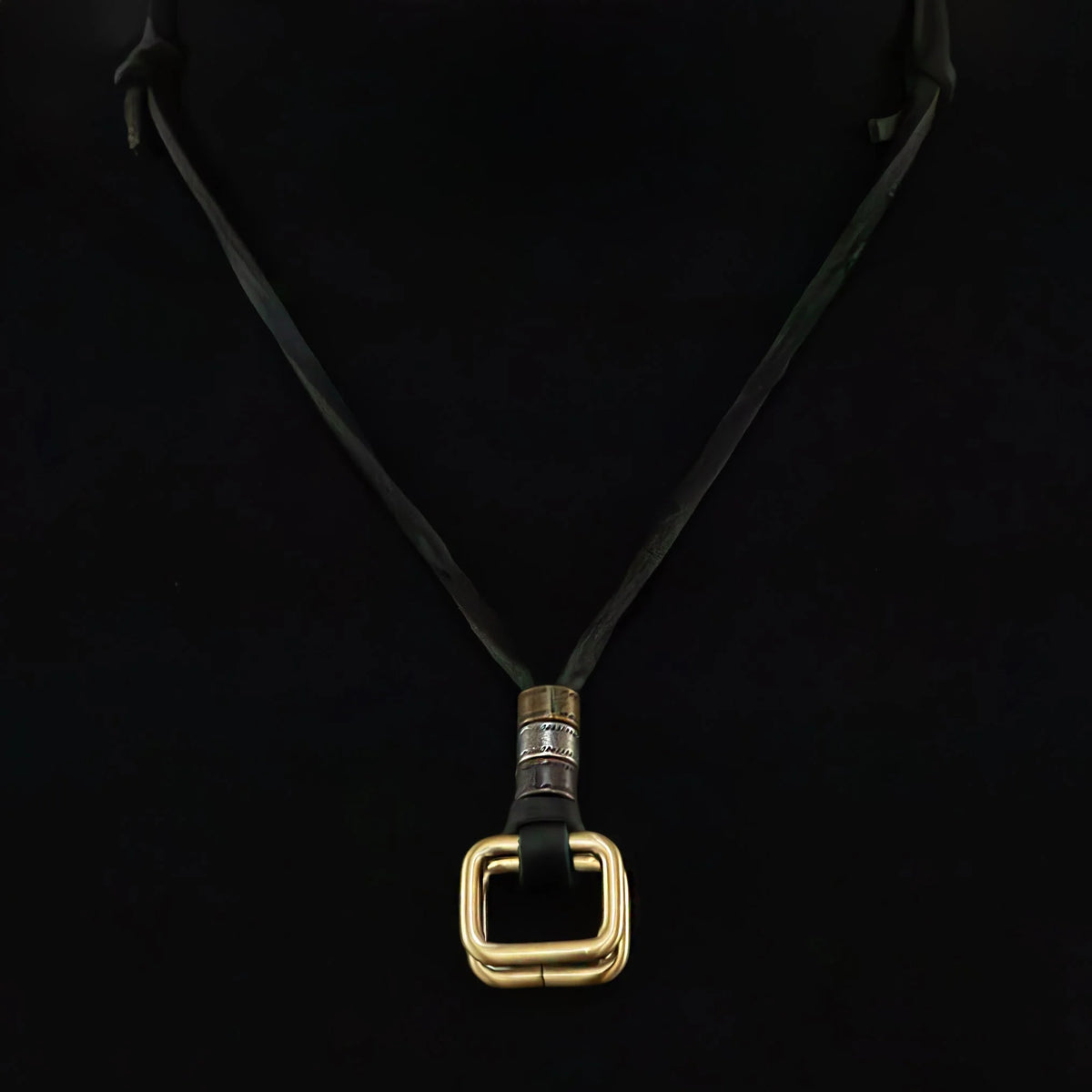 Necklace with a gold square pendant on a black cord.