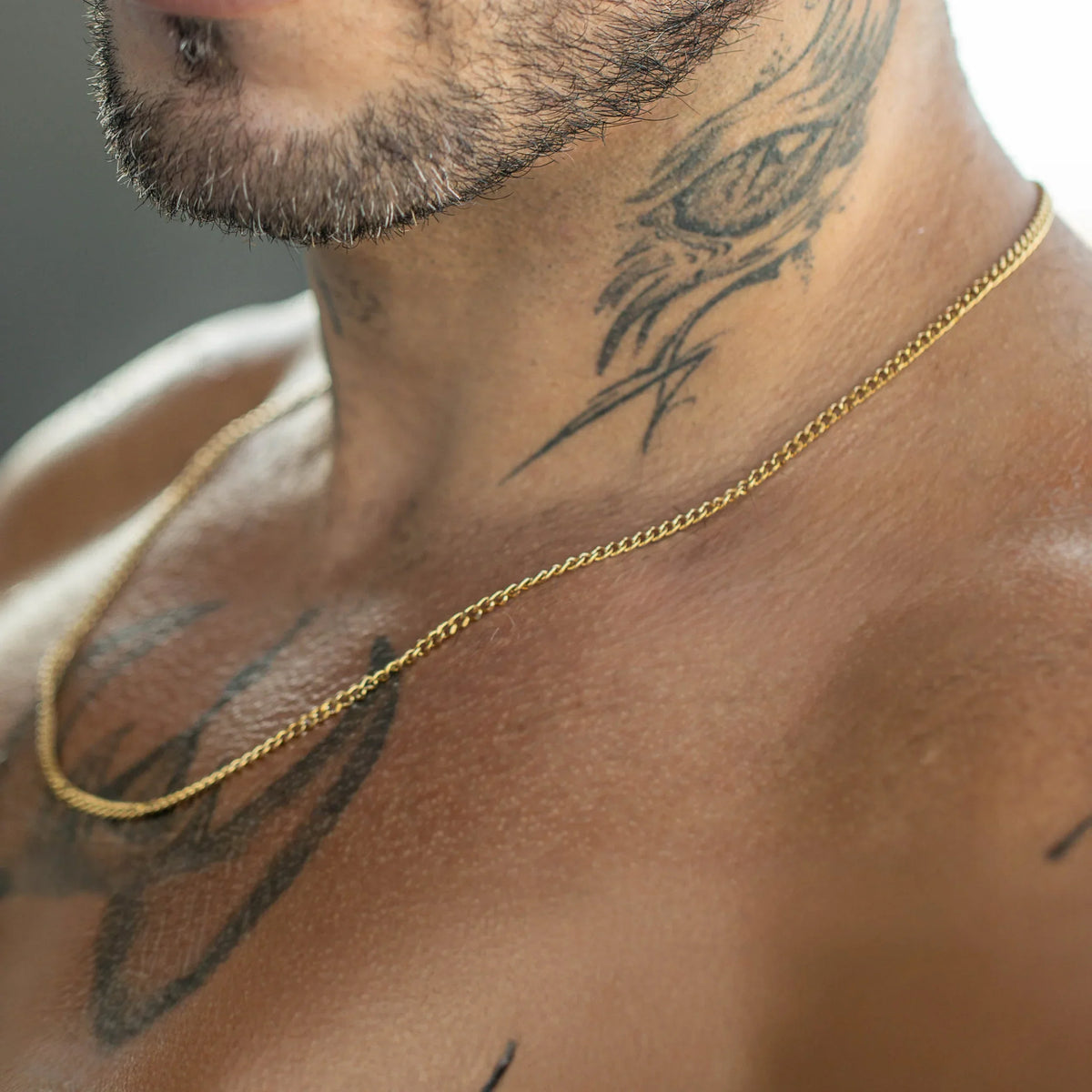 Gold chain necklace worn against tattooed skin.