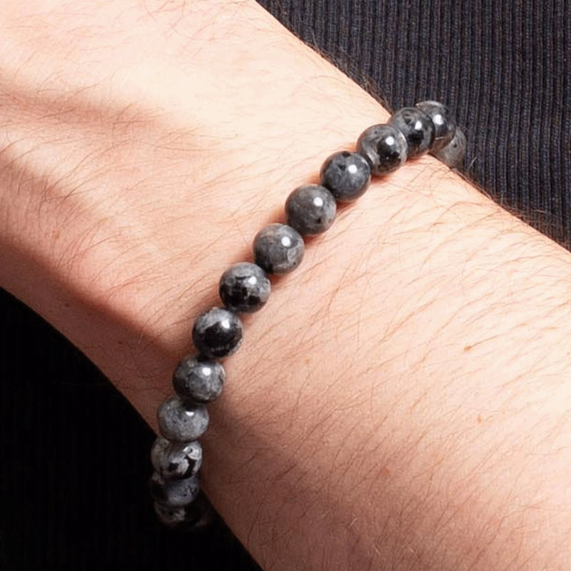 Bracelet made of dark gray, polished stone beads worn on a wrist.