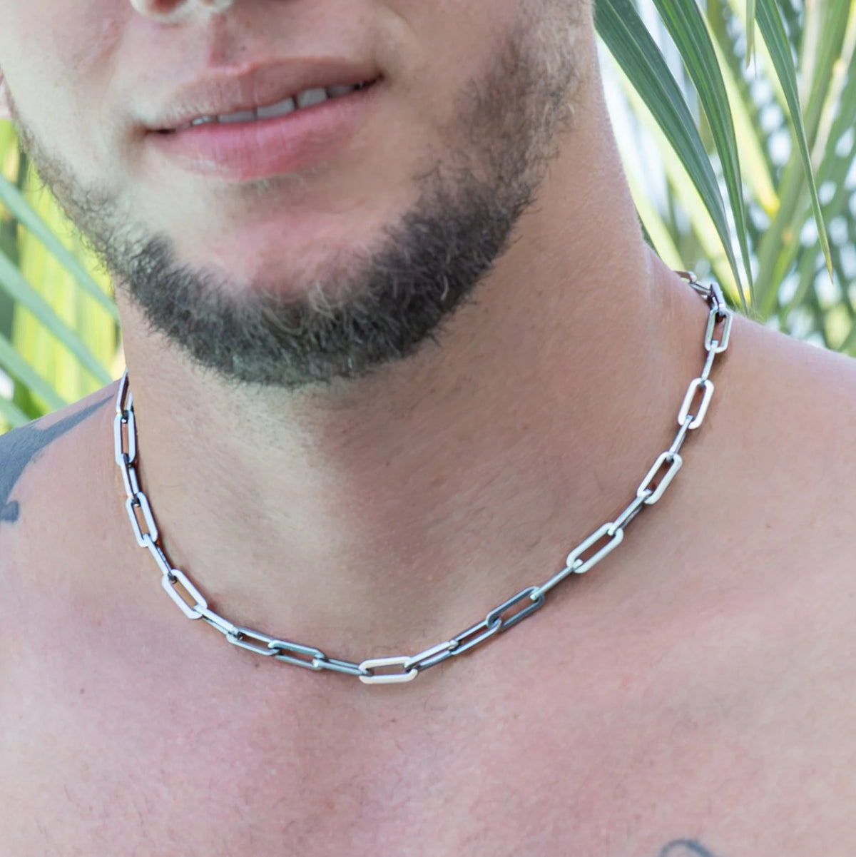 Silver chain necklace with elongated links worn around a neck.