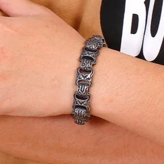 Metallic bracelet with intricate linked design worn on a wrist.