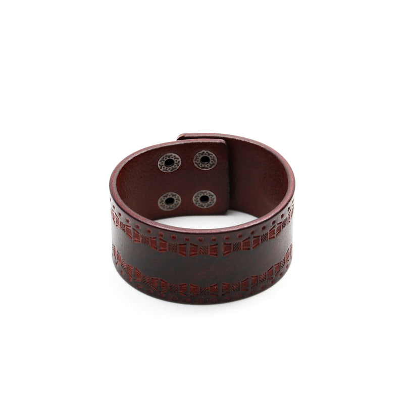 Wide brown leather bracelet with decorative cutout patterns and snap closures.