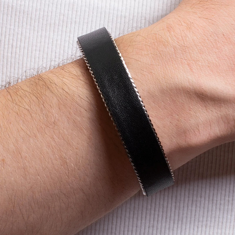 Black leather bracelet with stitched edges worn on a wrist.