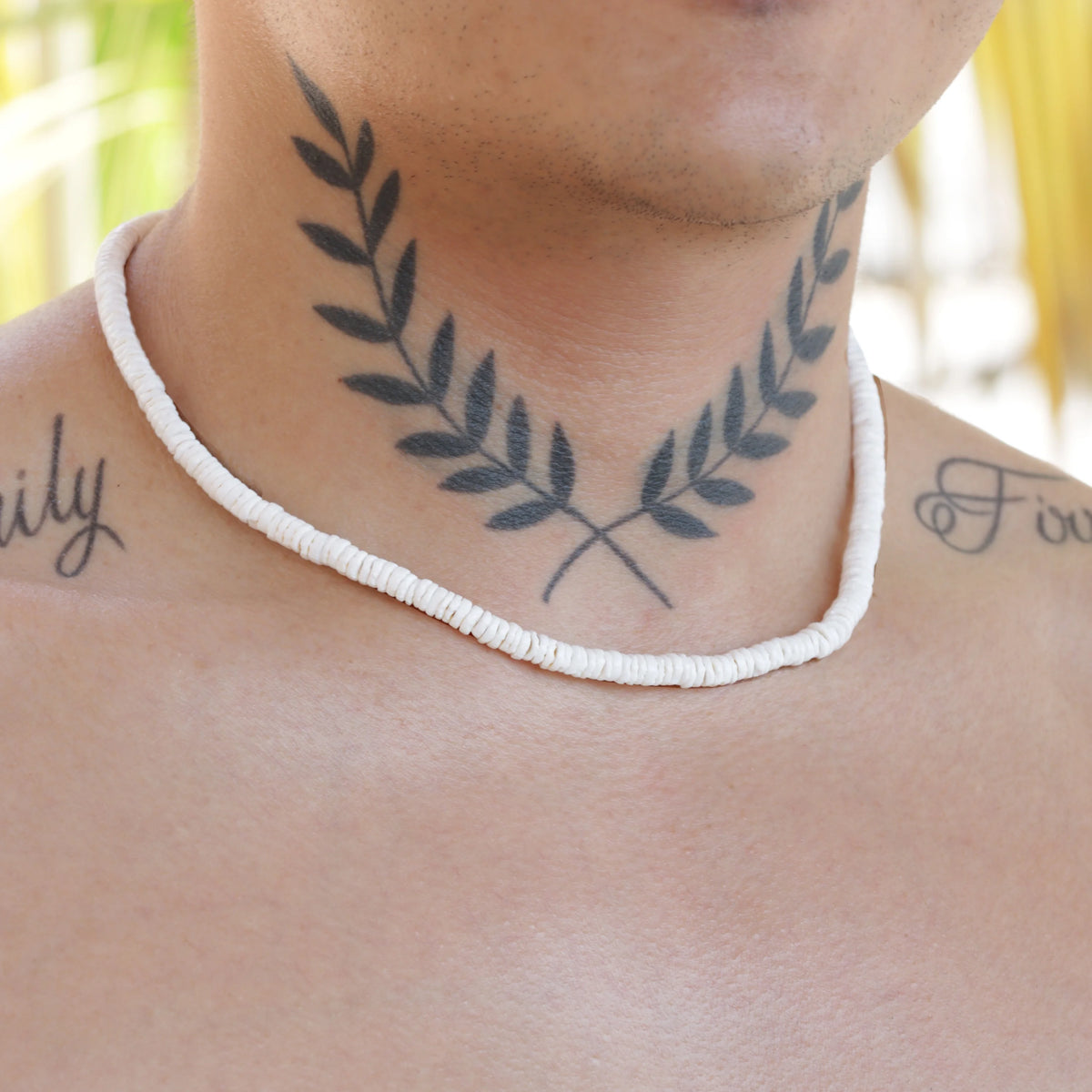 Tattoo of laurel leaves encircling the neck, accompanied by a white beaded necklace.