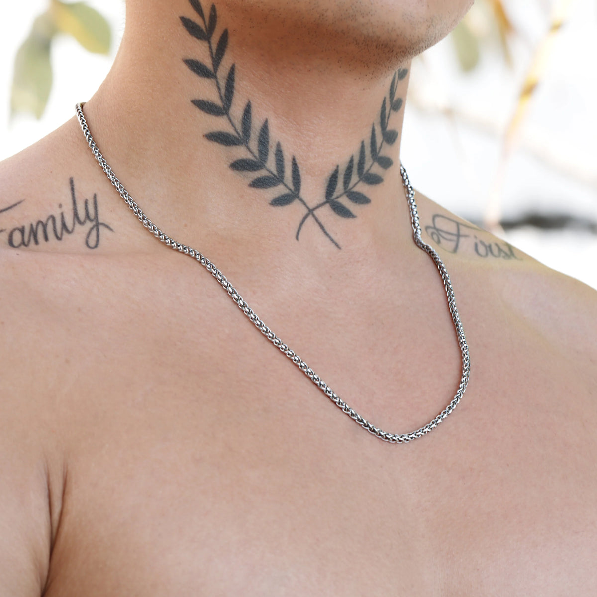 Silver chain necklace worn around a tattooed neck.