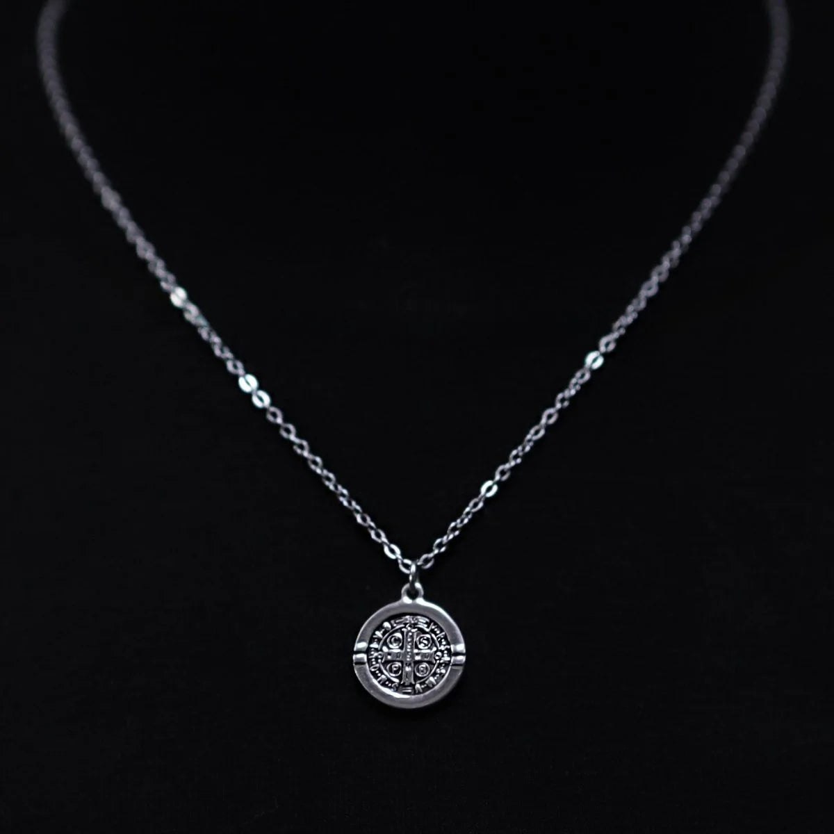 Silver necklace with a circular pendant featuring an ornate cross design.