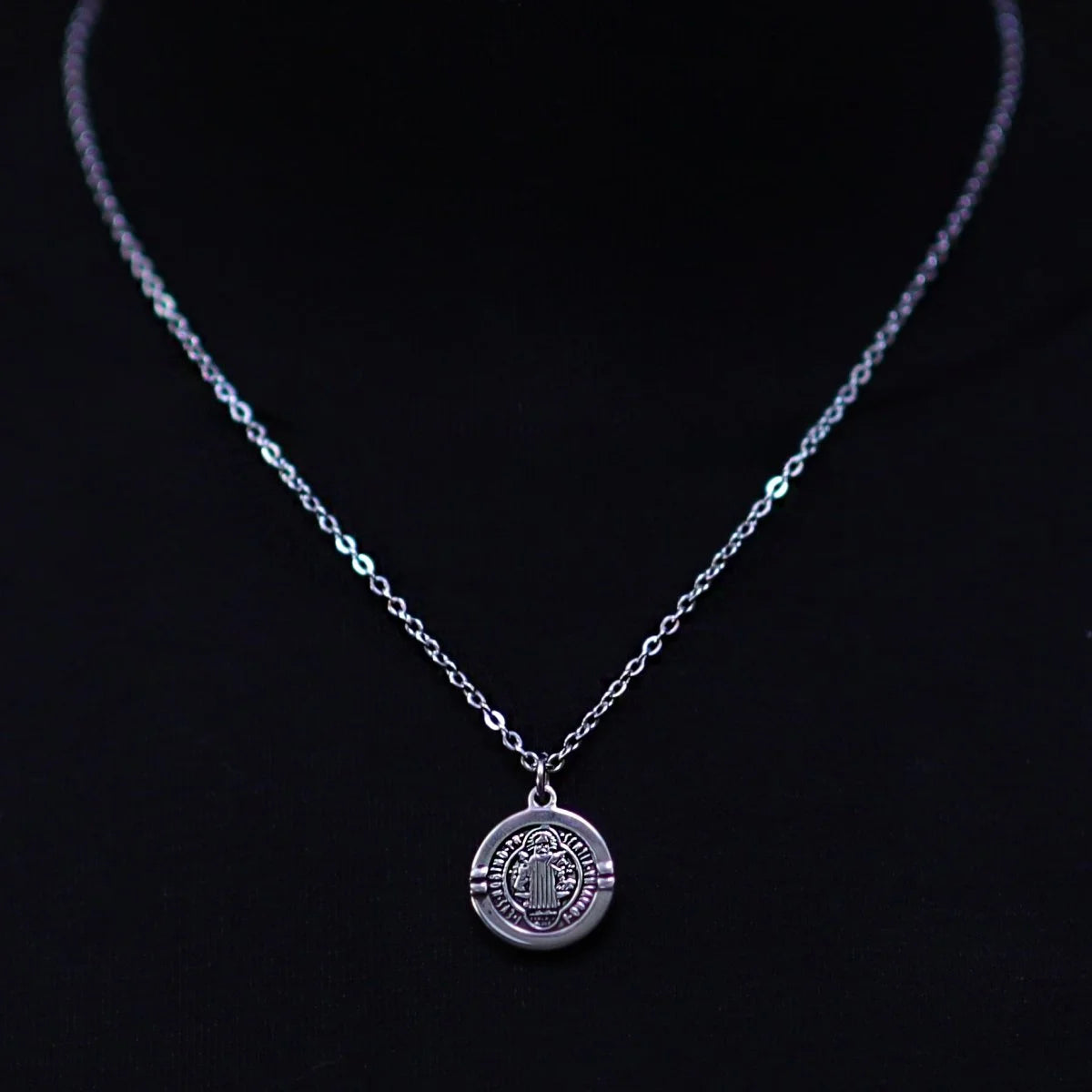 Silver necklace with a circular pendant featuring a religious medallion design.