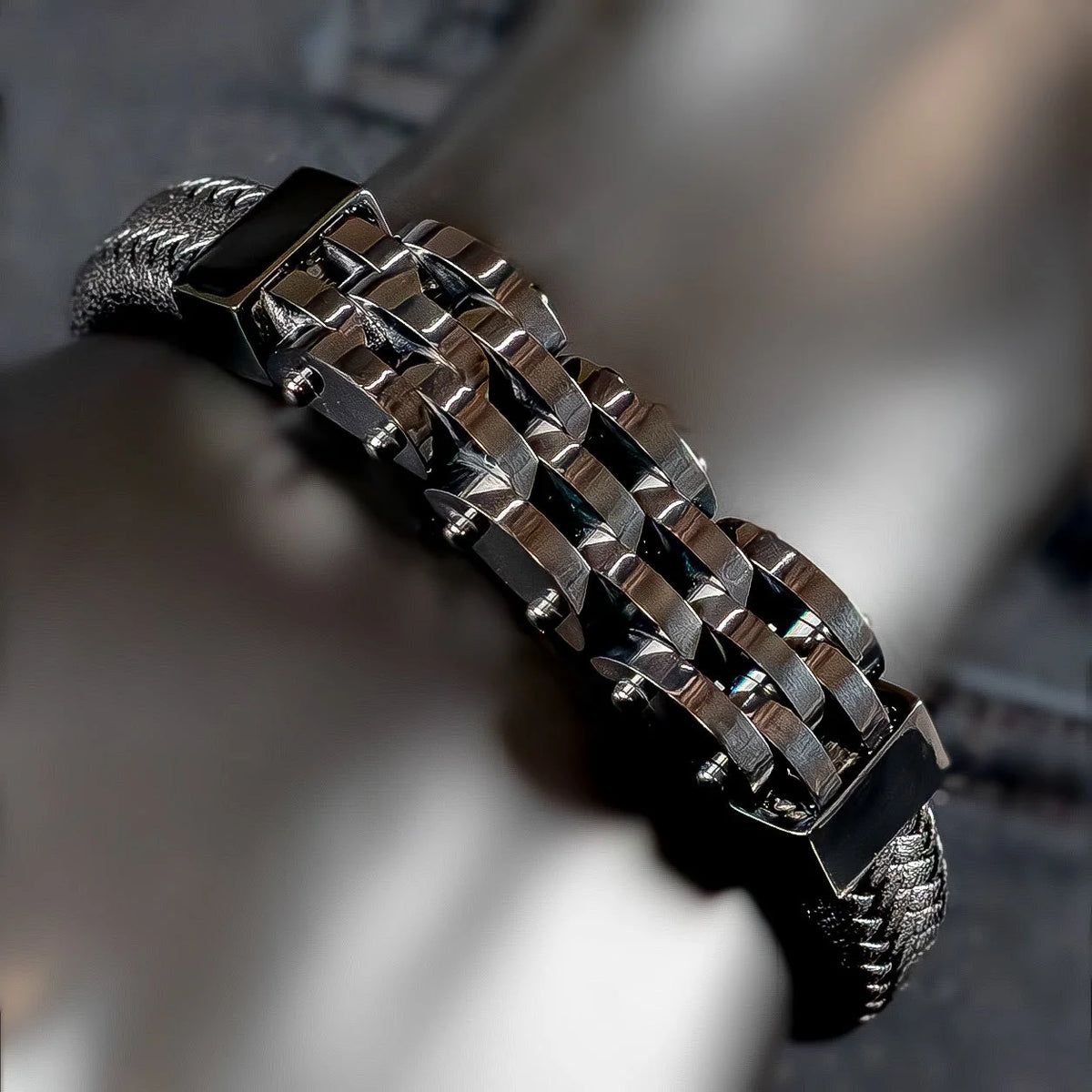 Metallic bracelet with interlocking geometric links on a black leather band.