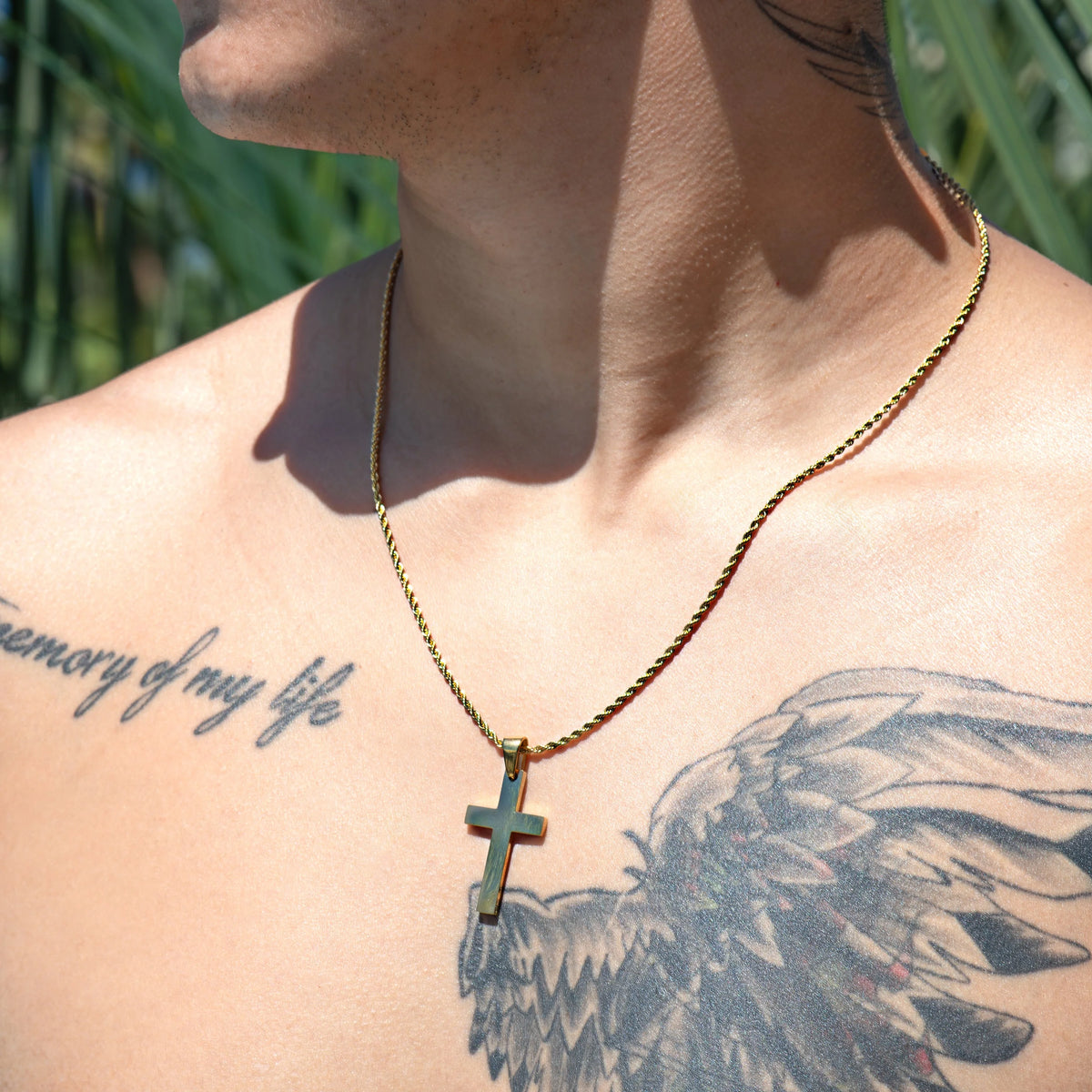 Gold chain necklace with a cross pendant worn over tattooed skin.