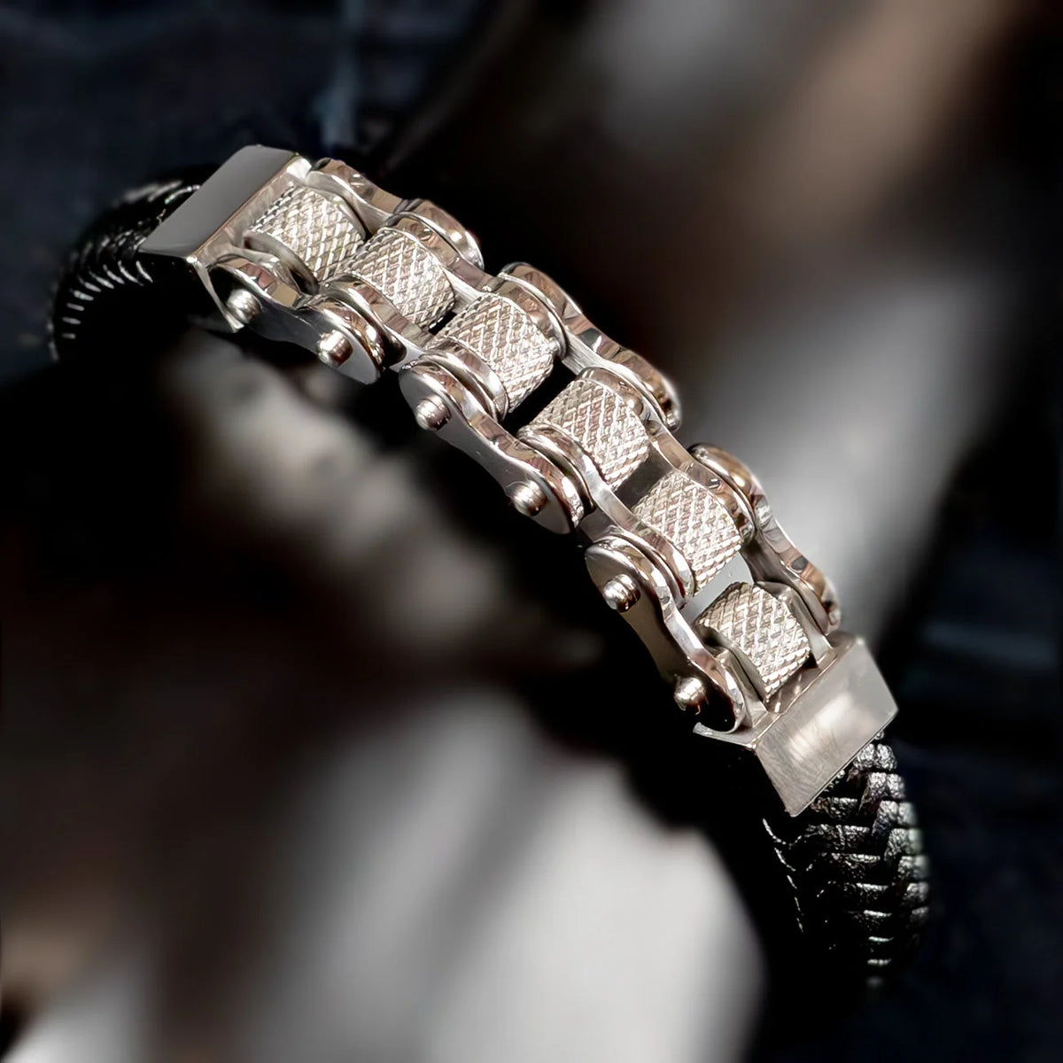 Silver-toned metal bracelet with textured links and a black cord base.