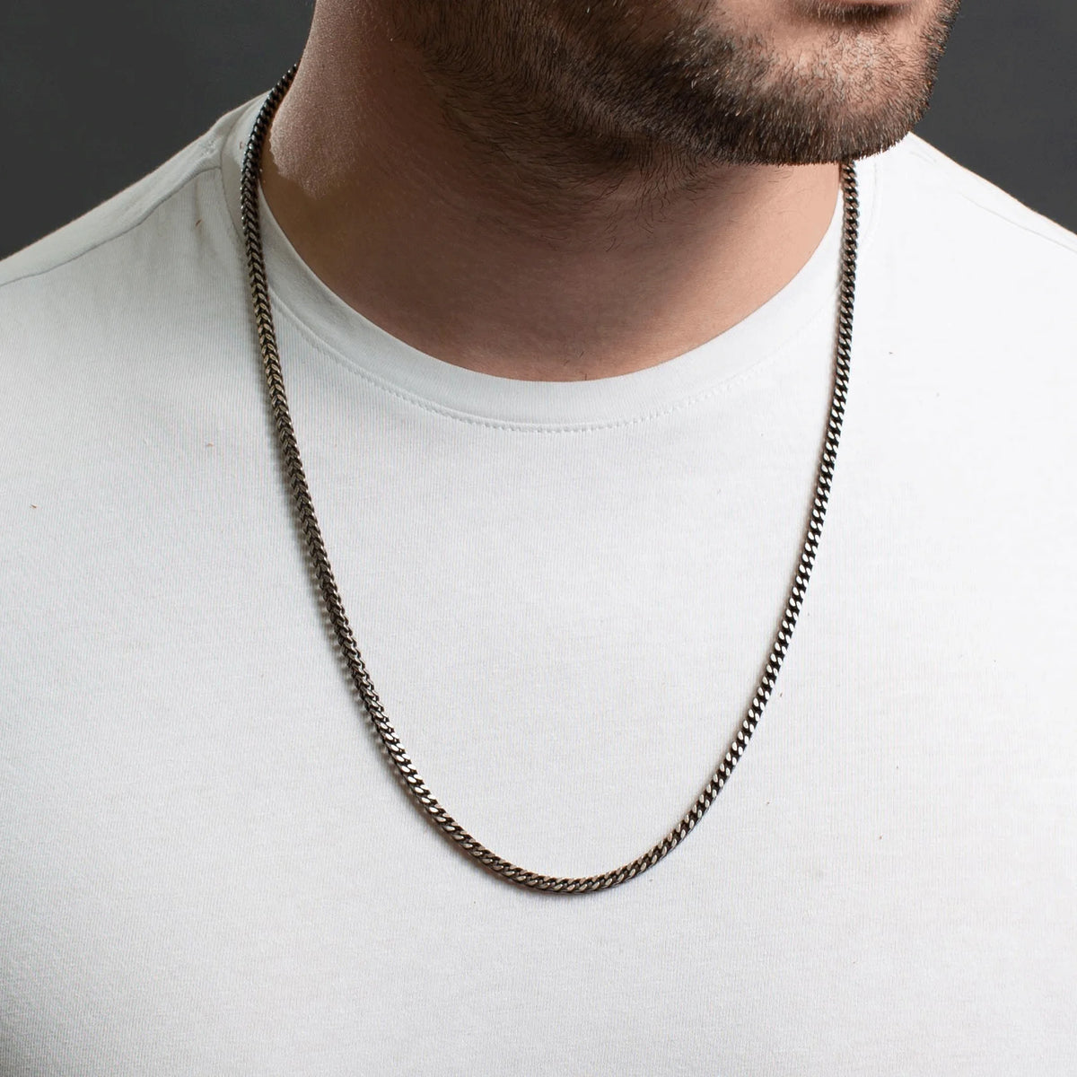 Silver chain necklace worn over a white t-shirt.