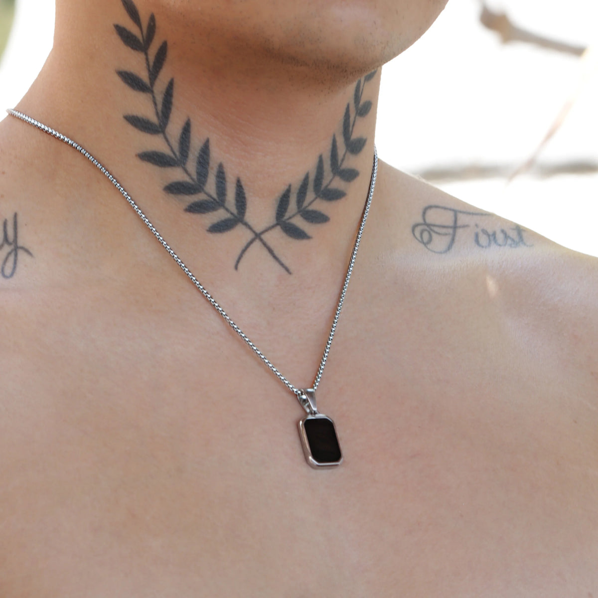 Tattoo of crossed laurel branches on a person’s neck, with a silver necklace and pendant visible.