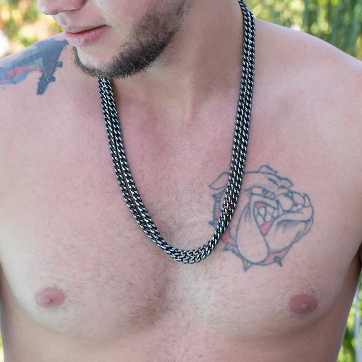 Heavy silver chain necklace worn by a man with visible tattoos on his chest and shoulder.