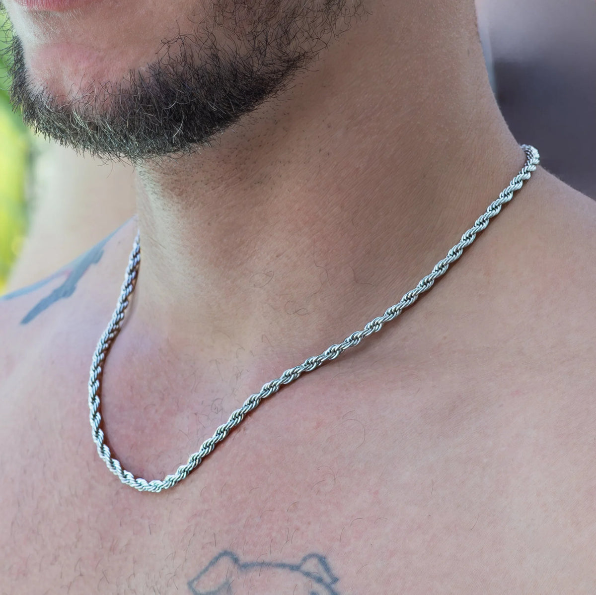 Silver twisted rope chain necklace worn around a person’s neck.