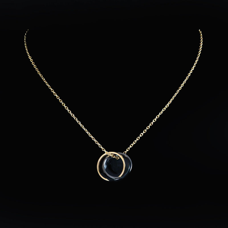 Gold necklace with a circular pendant featuring a dark stone or gem.