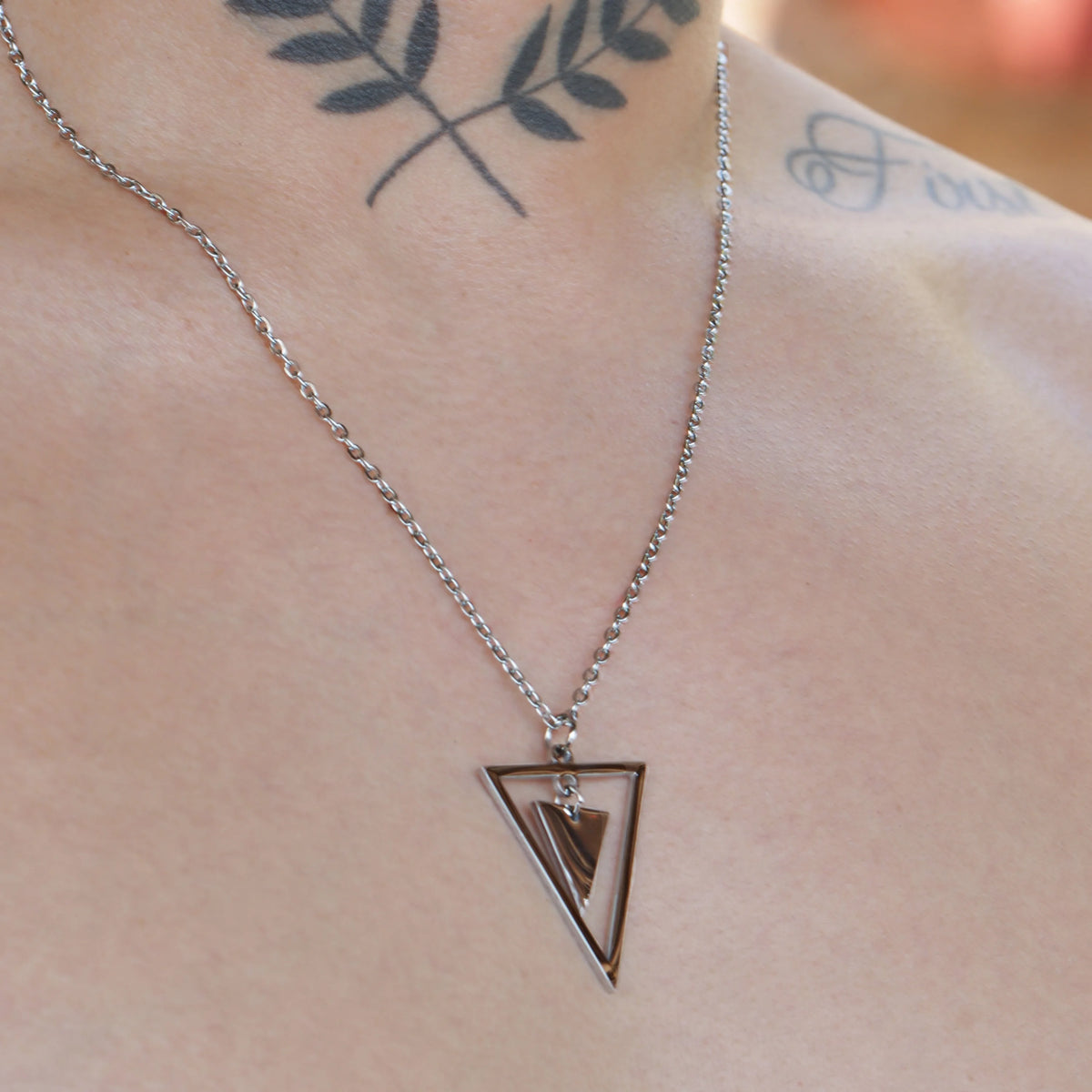 Silver triangular pendant necklace with geometric design.