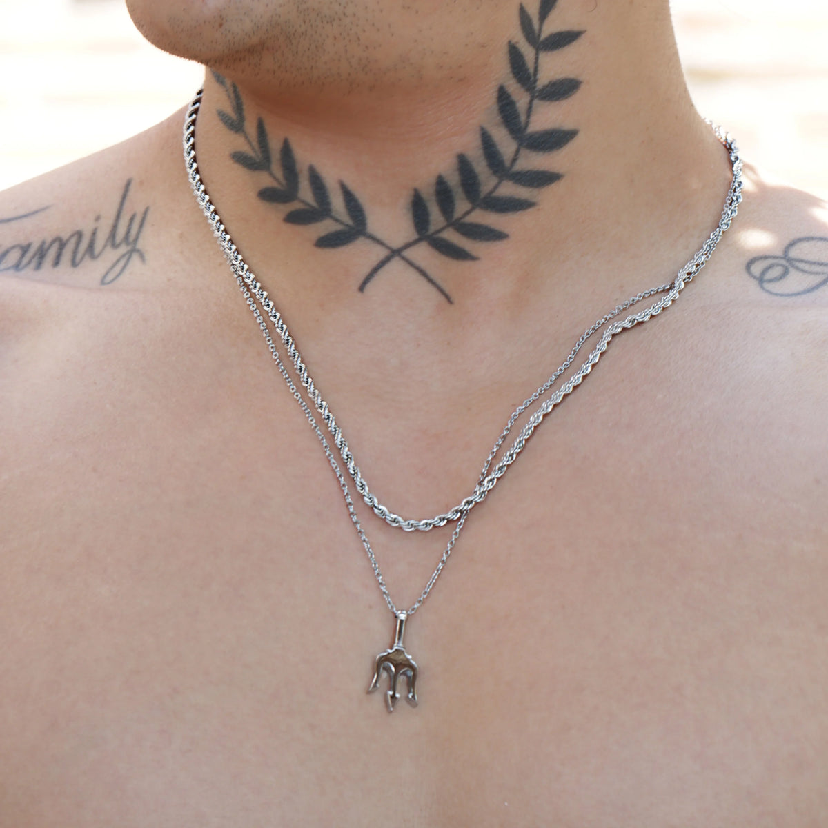 Silver layered necklace with a small elephant pendant and crossed laurel branch tattoo on the neck.