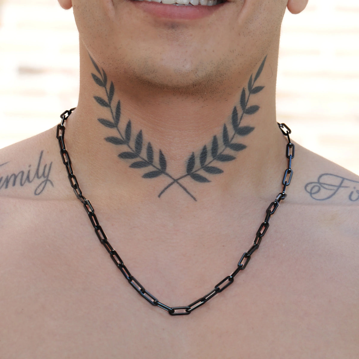 Crossed olive branches tattooed on a neck beneath a black chain necklace.