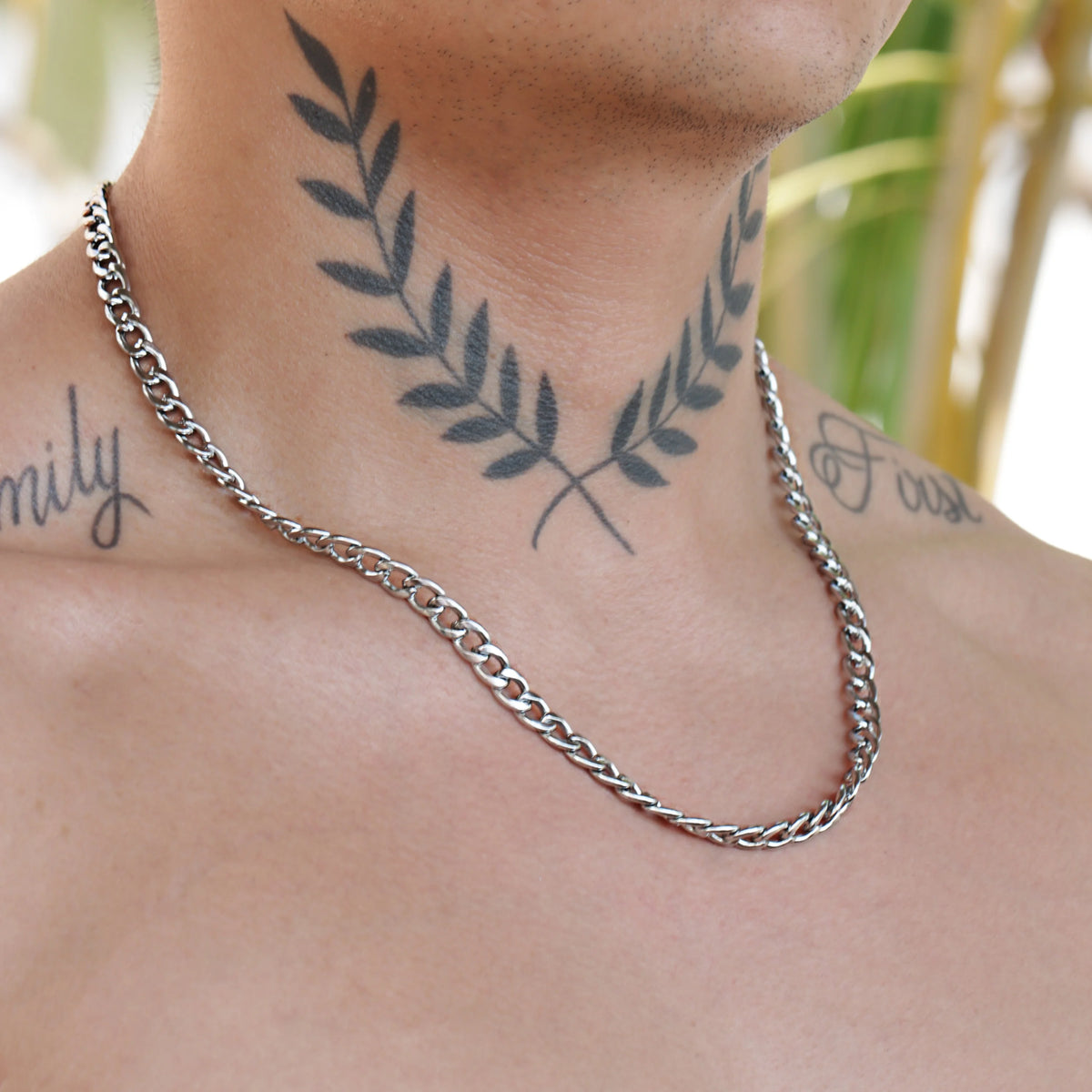 Silver chain necklace worn around a neck with visible tattoos.