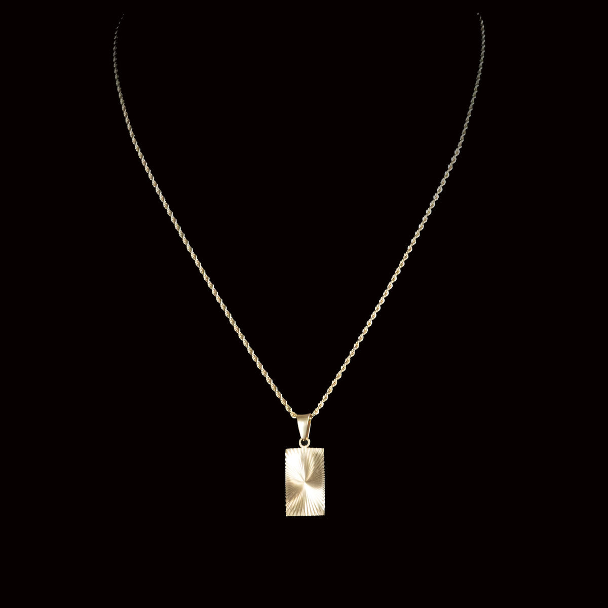 Gold necklace with a rectangular pendant featuring a sunburst pattern.