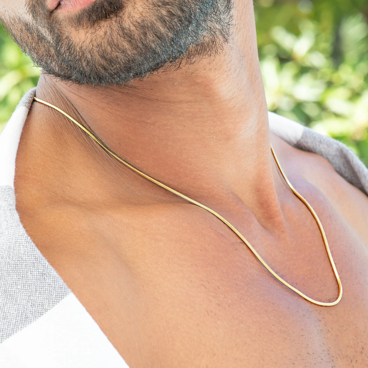 Thin gold chain necklace worn around a person’s neck.