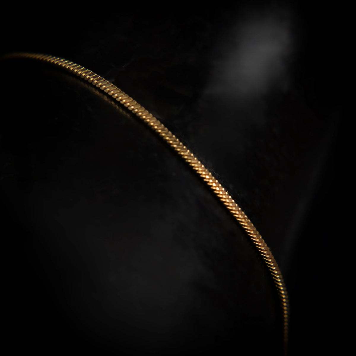 Curved golden chain or necklace against a dark background.