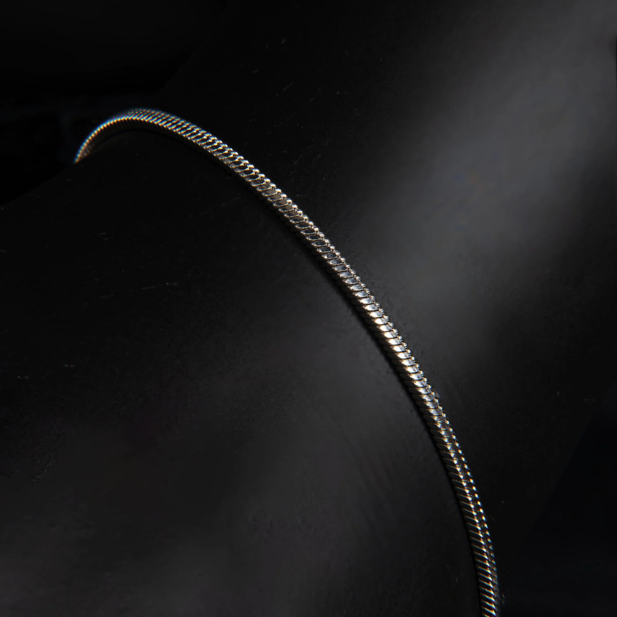 Curved, metallic chain or cable with a reflective surface against a dark background.