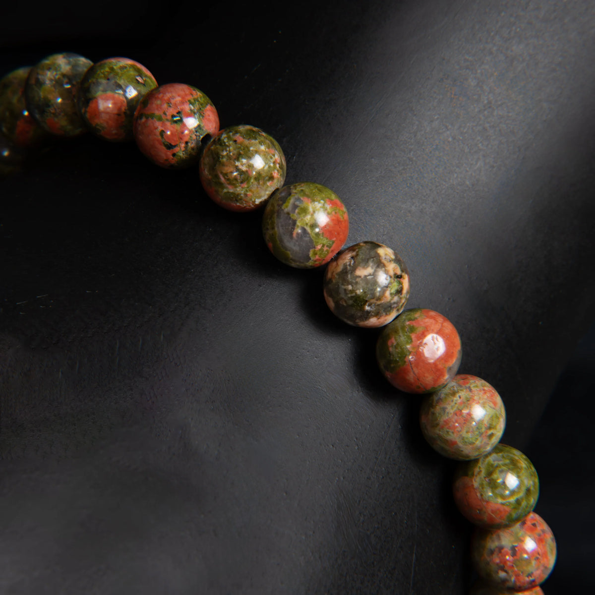 Curved string of multicolored, speckled beads against a dark background.