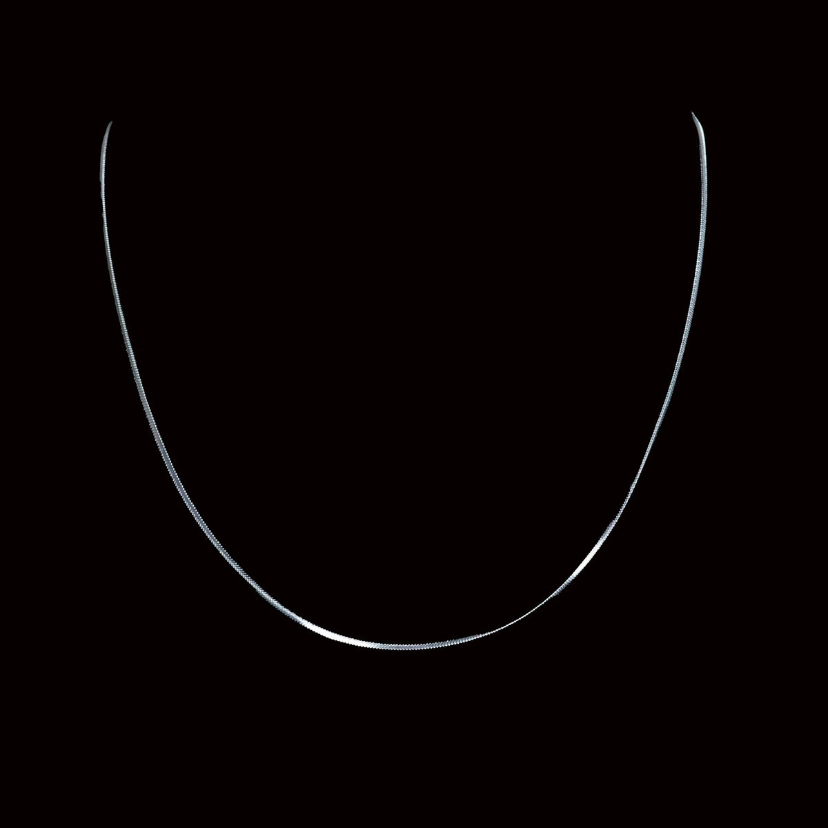 Thin, curved silver necklace chain against a black background.