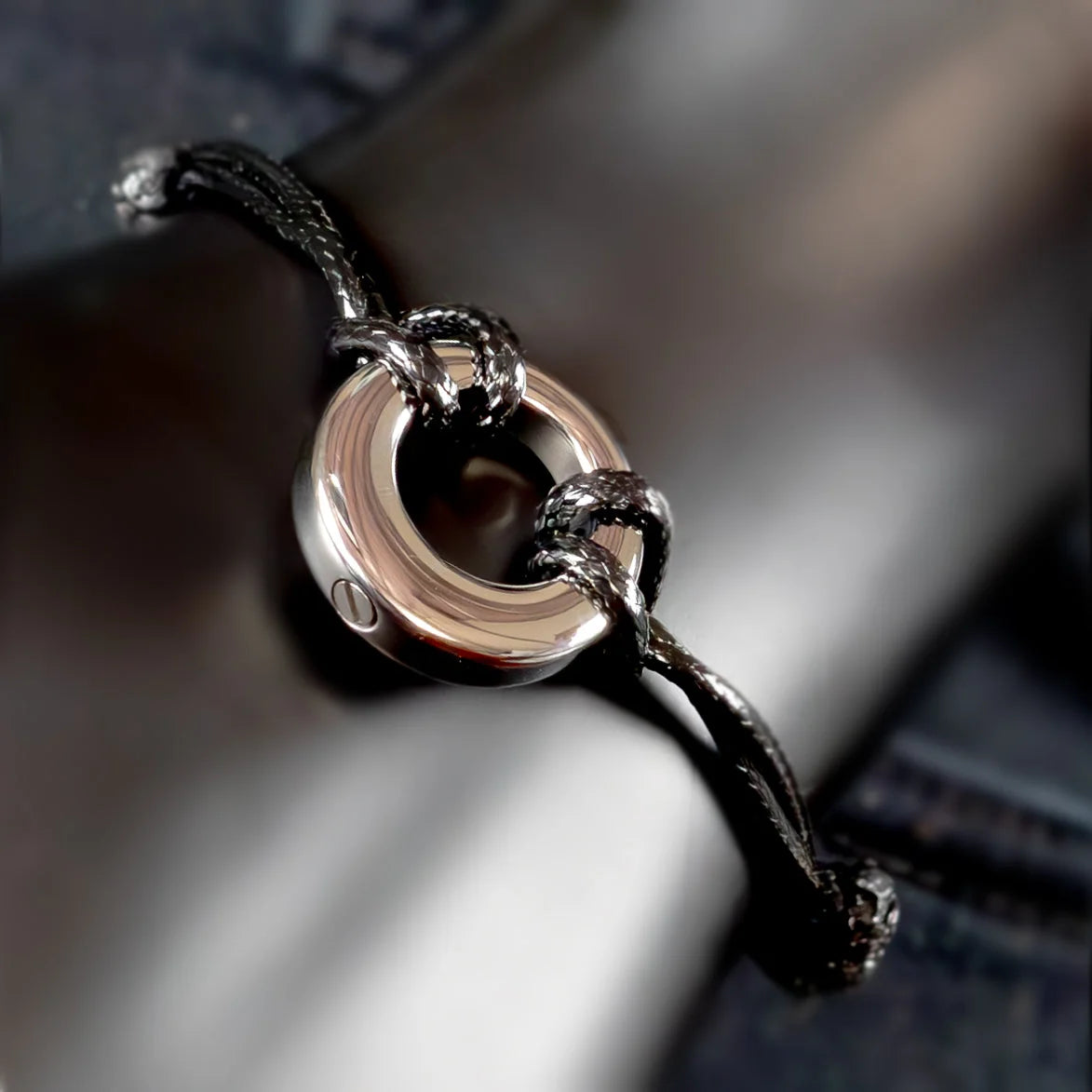 Circular silver pendant on a black cord bracelet.