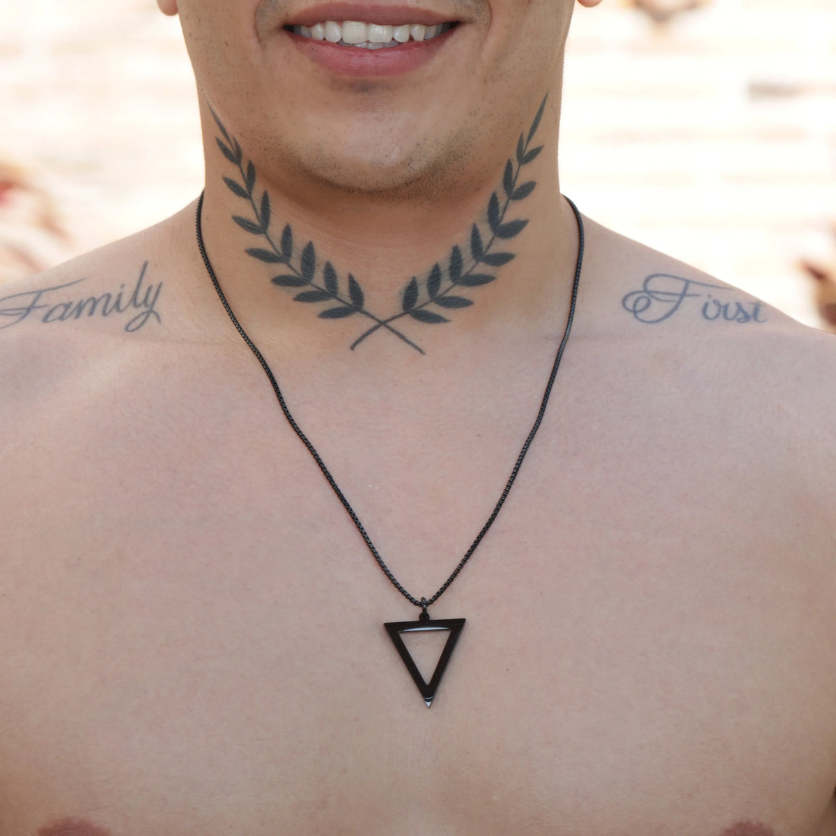 Triangular pendant necklace on a black cord with laurel leaf tattoos visible beneath.