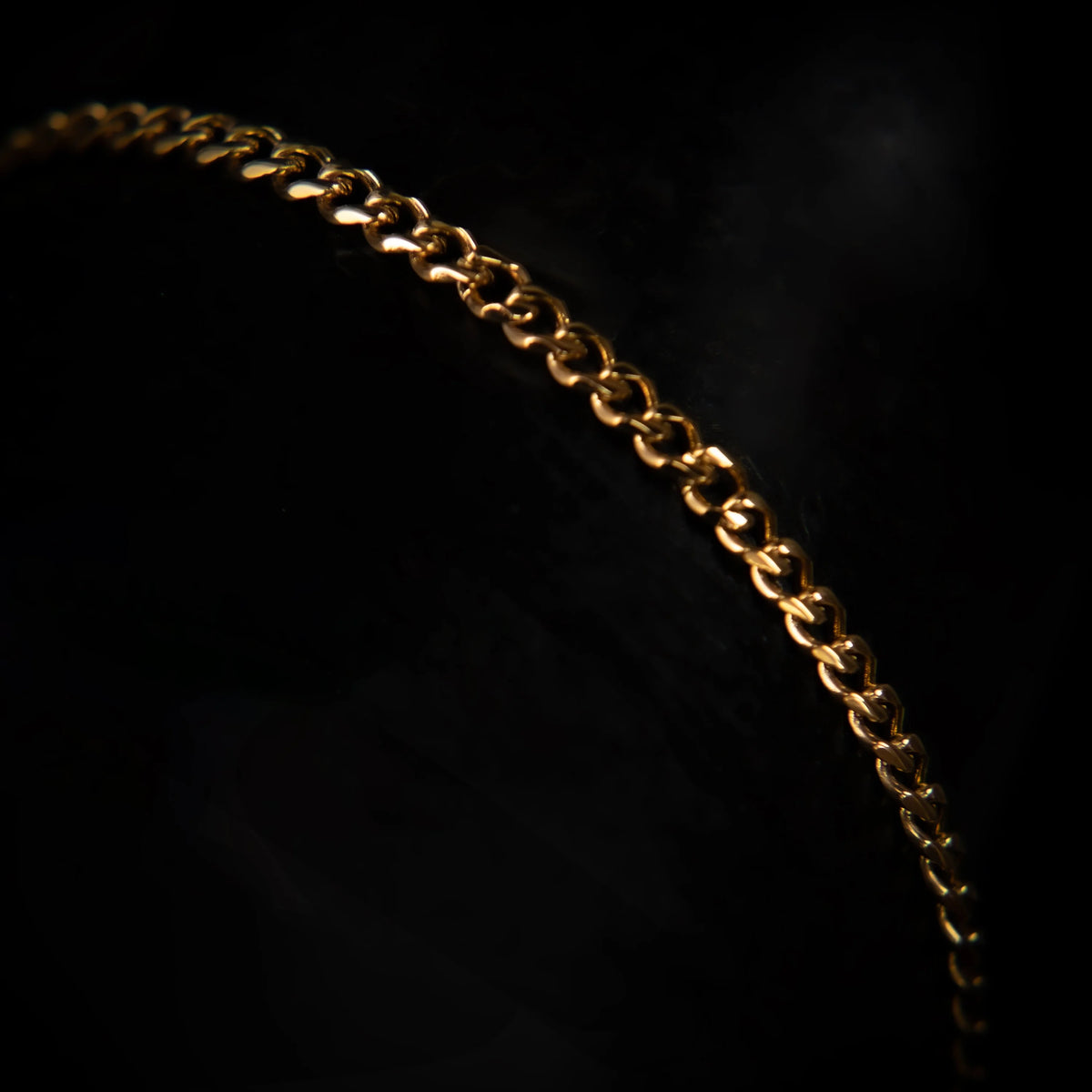 Delicate gold chain curving against a dark background.