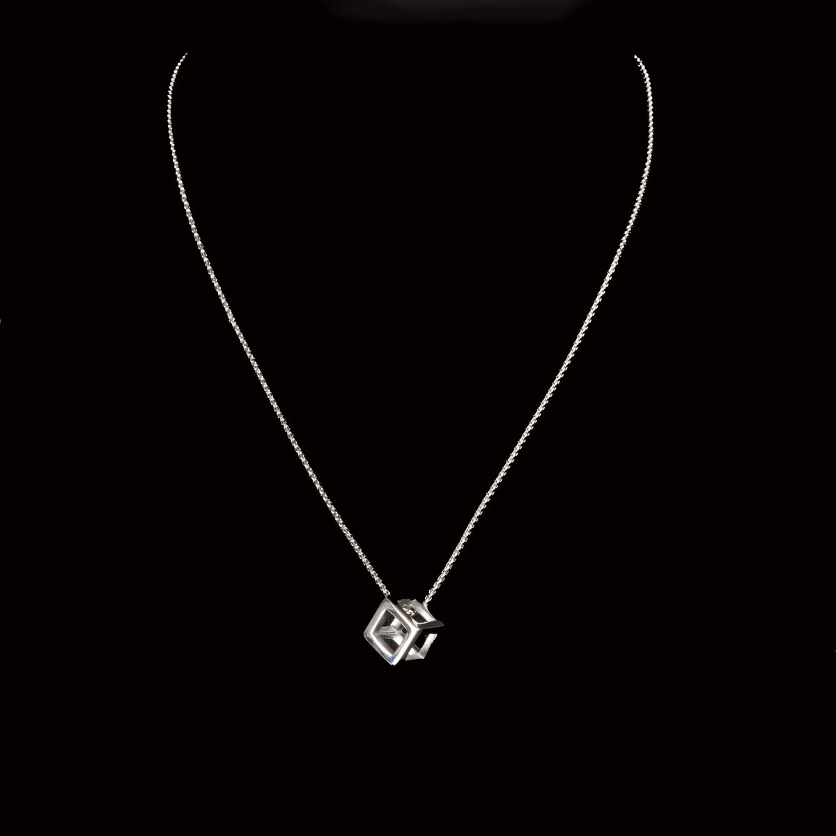 Silver necklace with a geometric cube-shaped pendant.