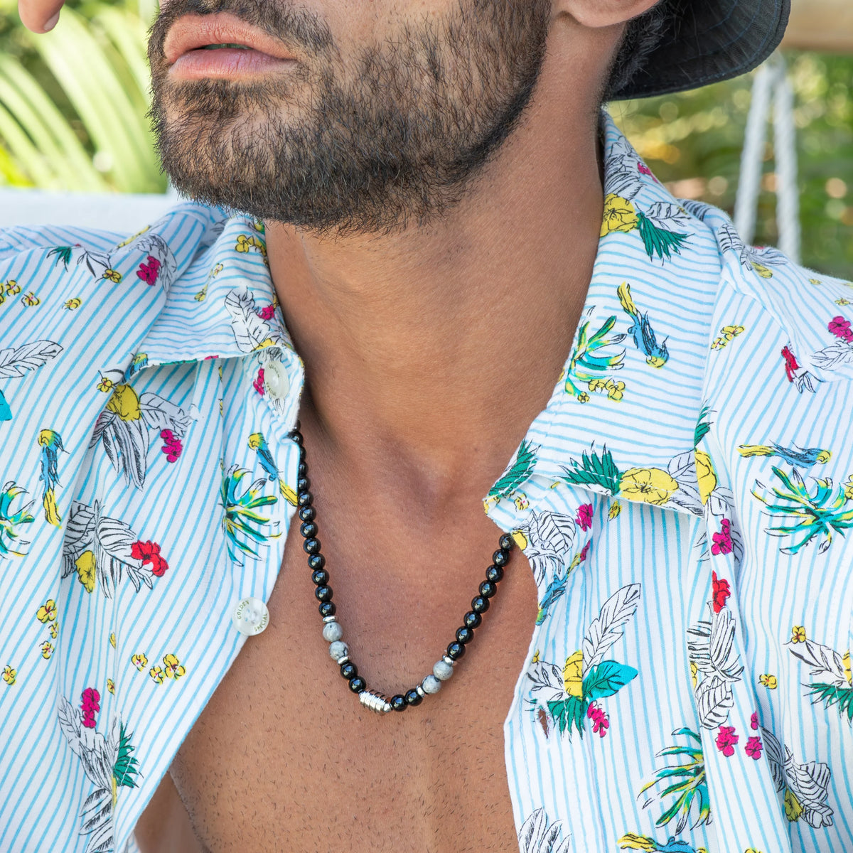 Colorful tropical print shirt with floral and leaf patterns on a light blue striped background.