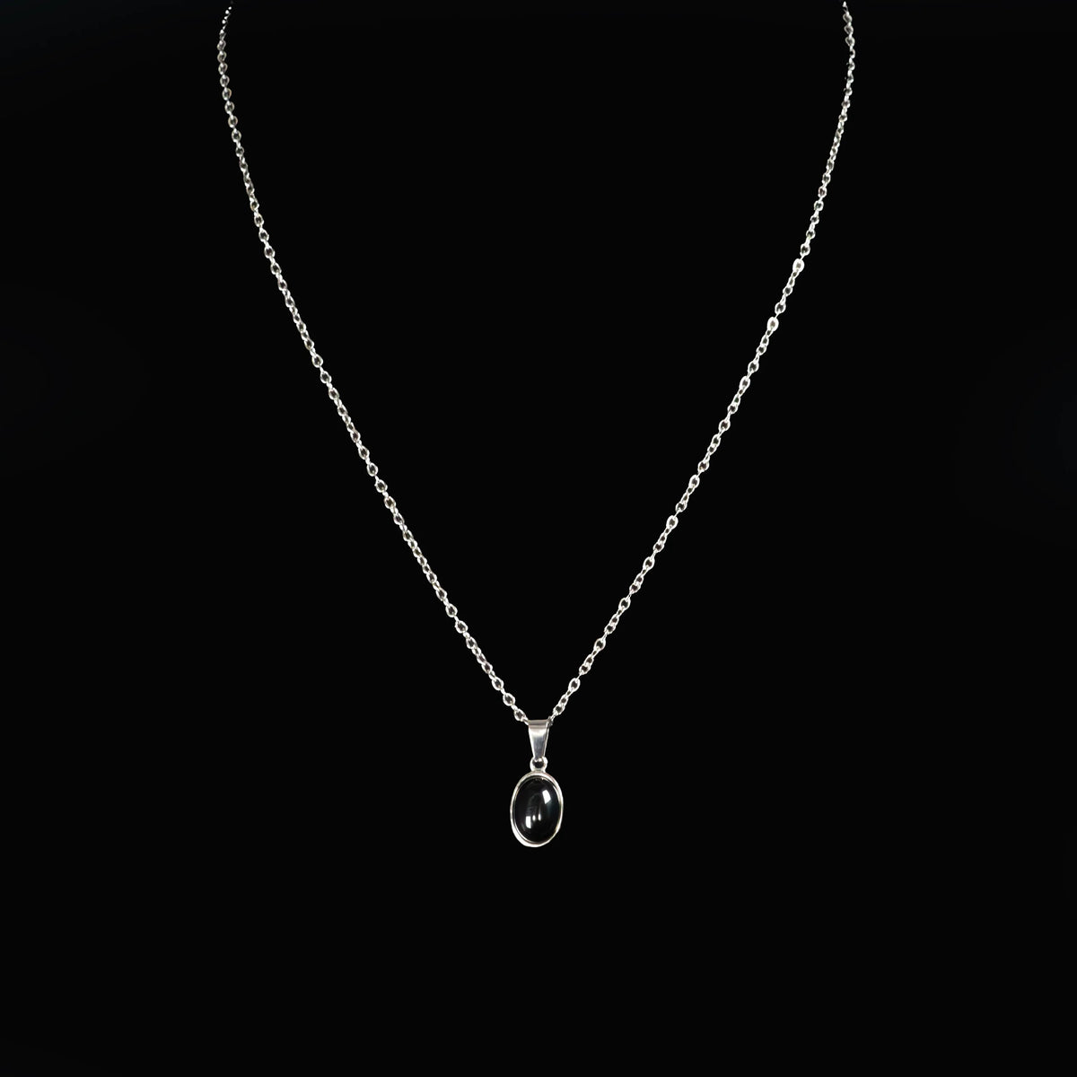 Silver necklace with an oval pendant containing a dark gemstone.