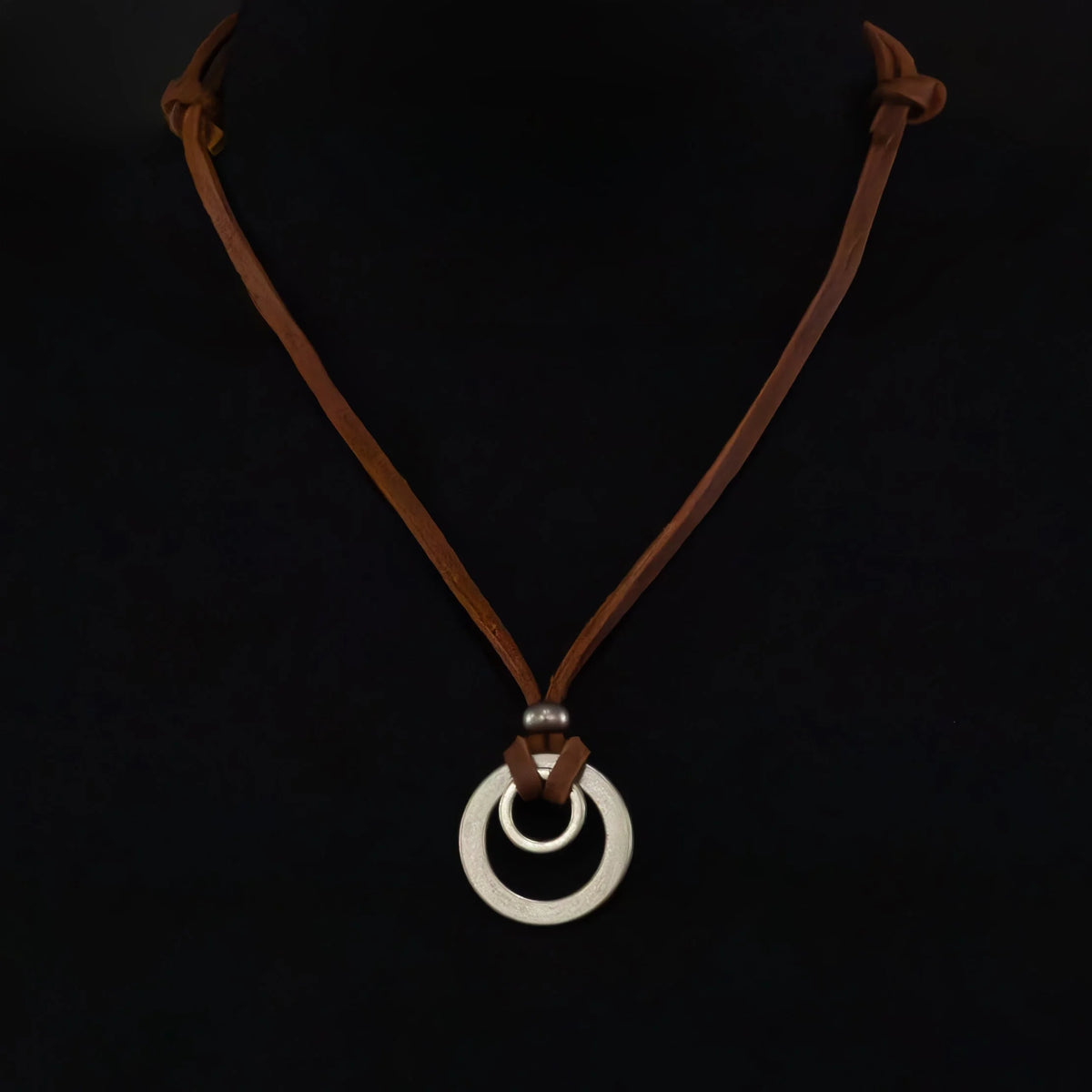 Leather necklace with a white circular pendant.