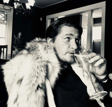 A person wearing a fur coat while drinking from a cocktail glass.