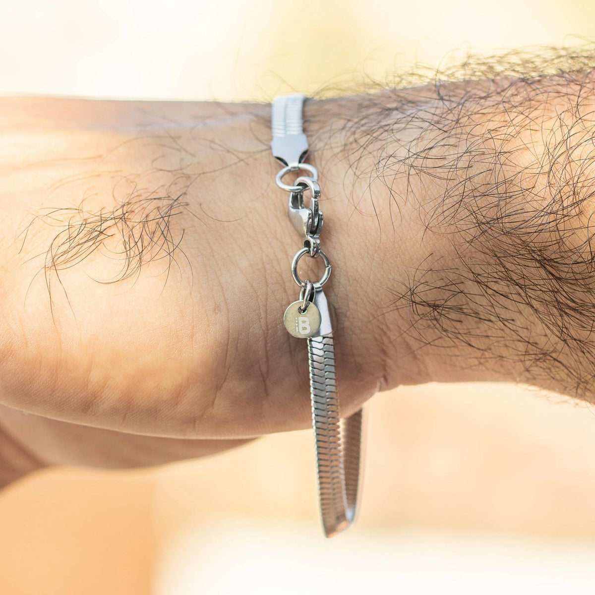 Metal nail file charm hanging from a white cord bracelet.