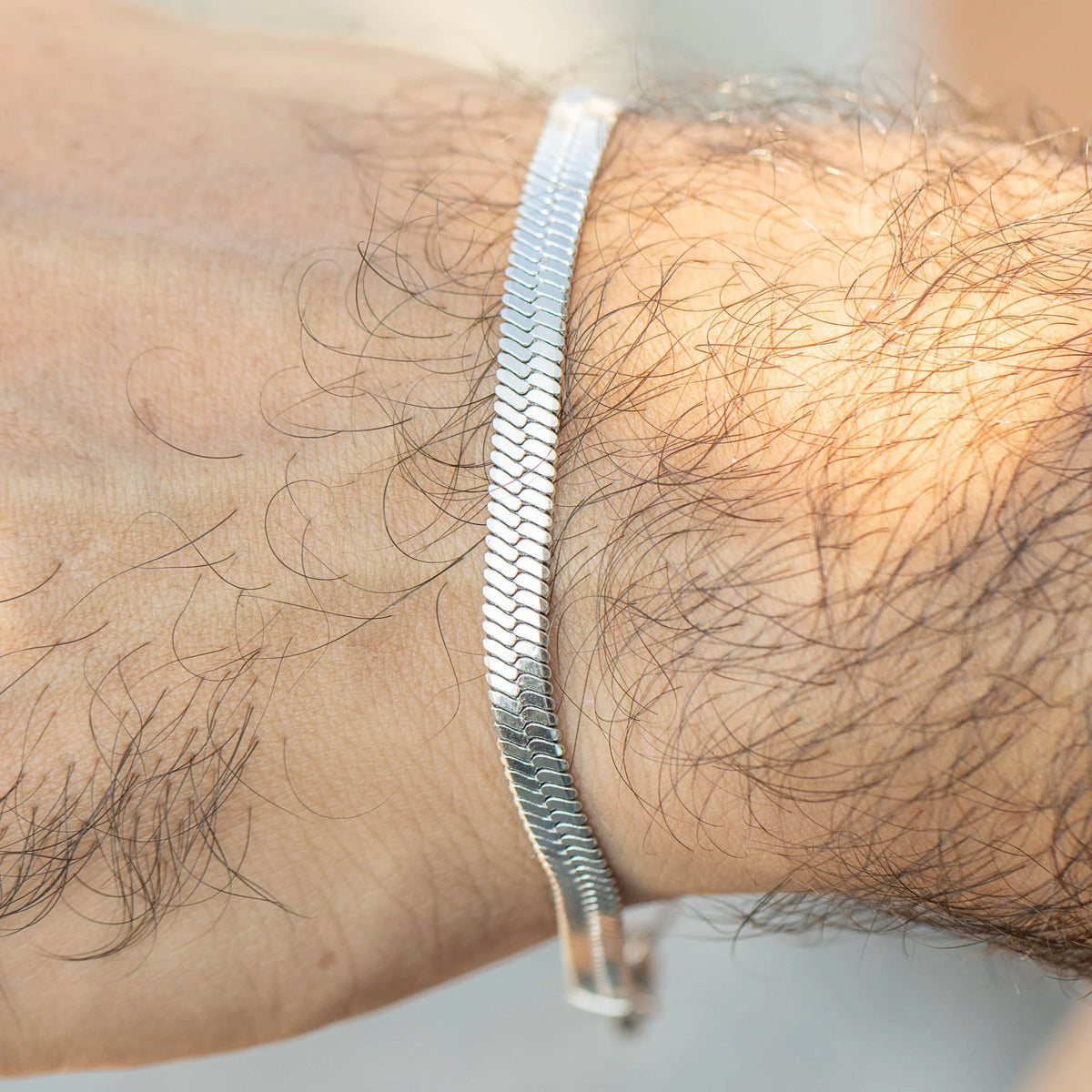 Silver herringbone chain bracelet worn on a wrist.