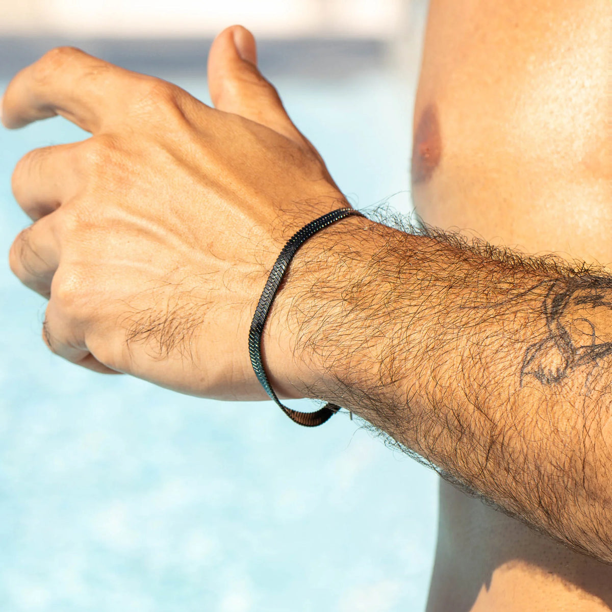 Simple black elastic hair tie worn as a bracelet on a tattooed wrist.