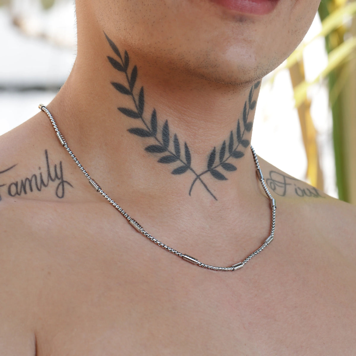 Tattoo of a laurel wreath design on a person’s neck and upper chest.