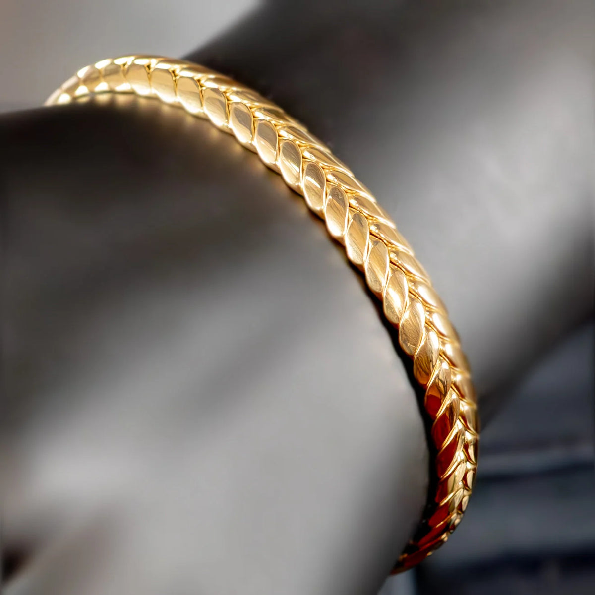 Gold bracelet with an intricate braided or woven pattern.