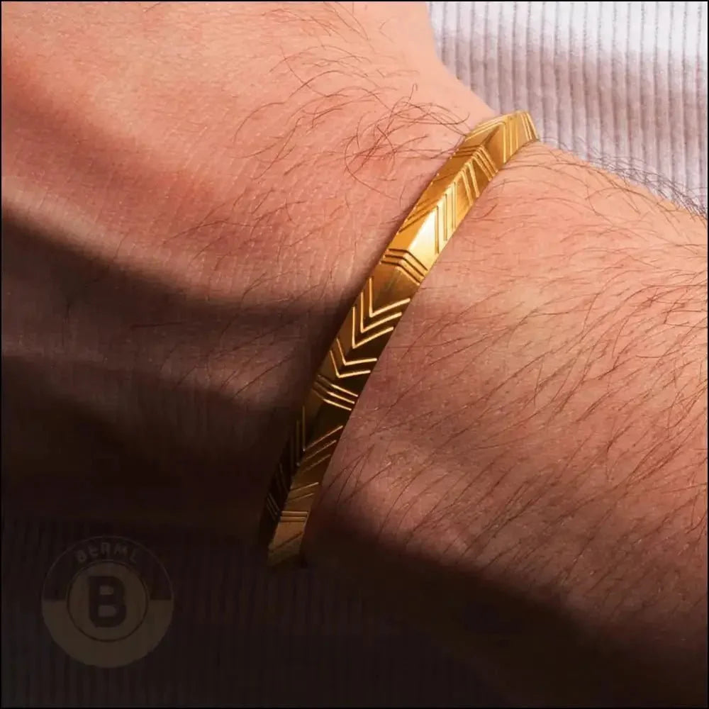 Gold bracelet with chevron pattern engraved on its surface.