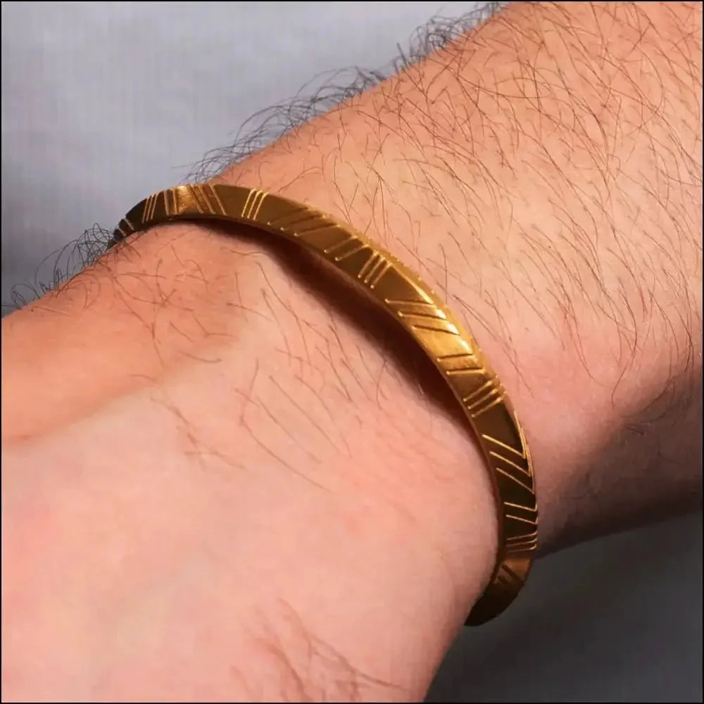 Gold bracelet with engraved linear patterns worn on a wrist.