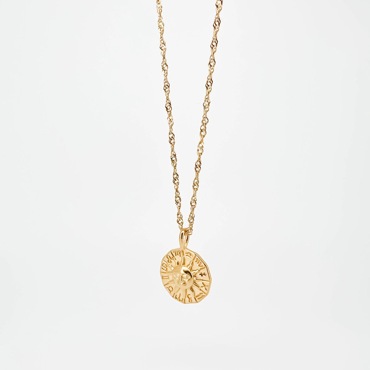 Gold pendant necklace featuring a circular medallion with a sun design.